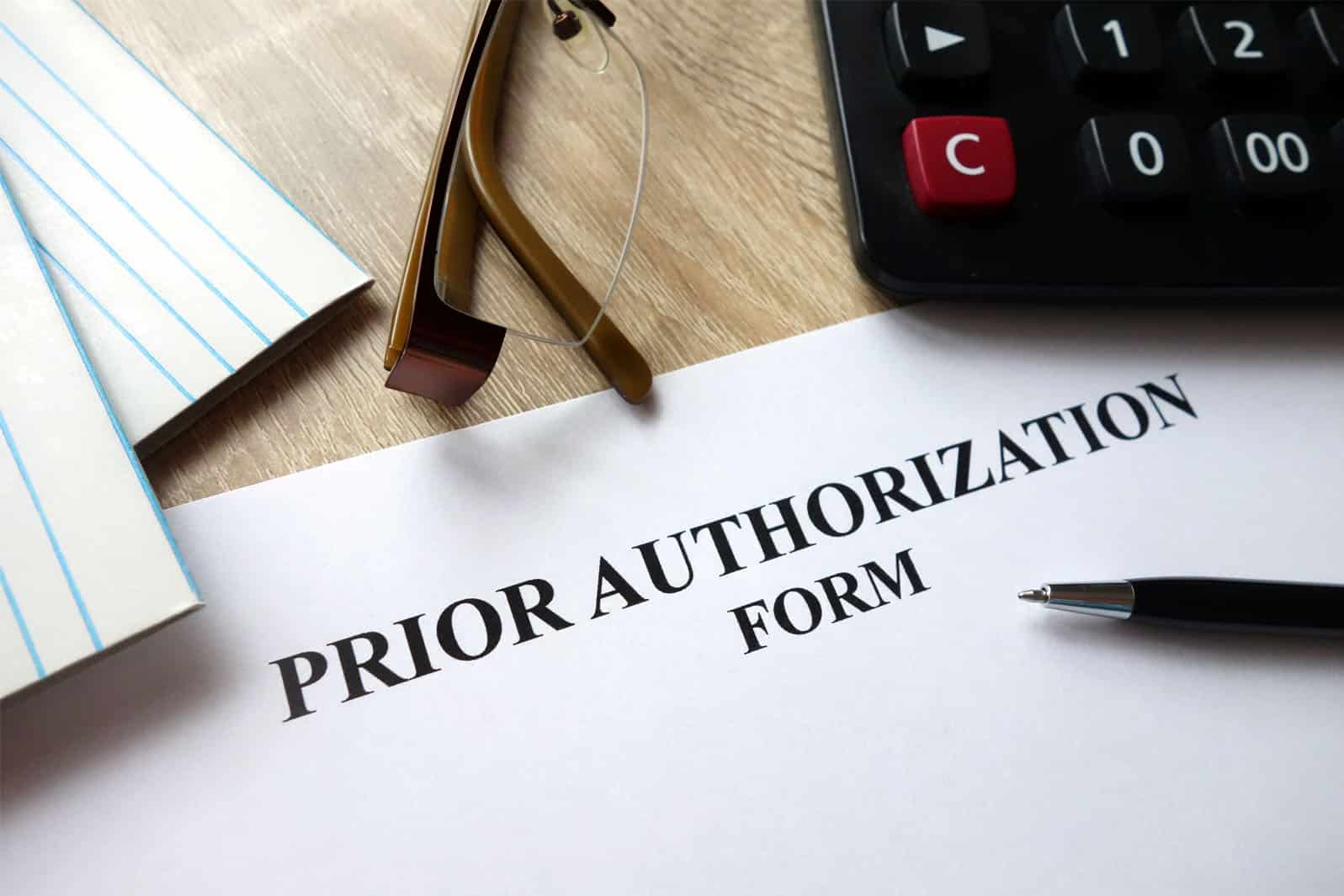 Prior authorization from on desk near calculator and pen.