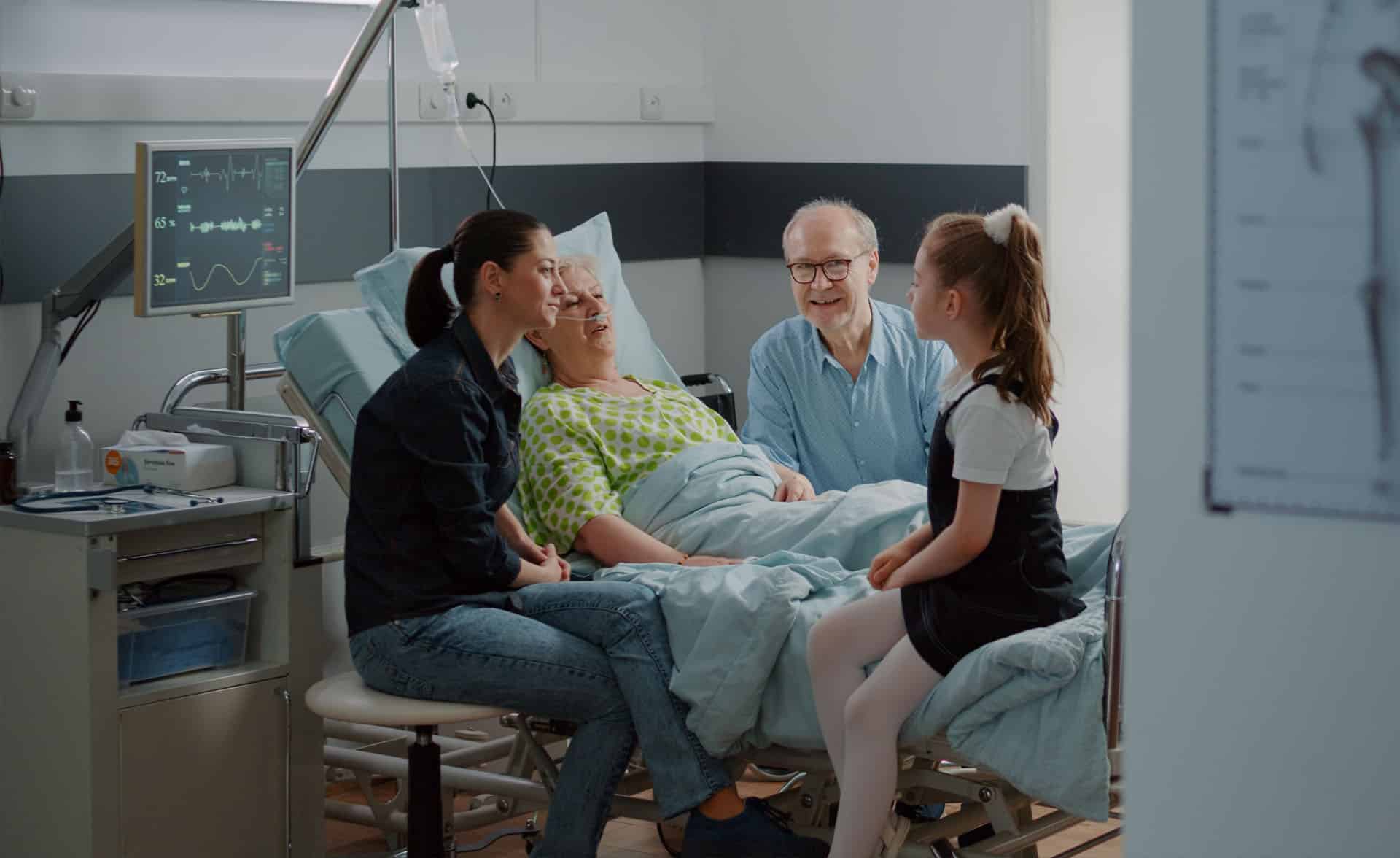 Young girl visiting aged woman in hospital ward bed with mother and old man
