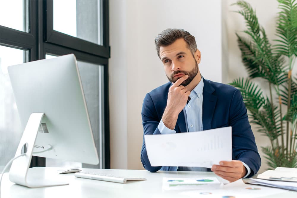 Pensive thoughtful caucasian businessman, corporate director, sits in the office at workplace, working with documents, looks away, thinking about project strategy, ideas, planning business plan