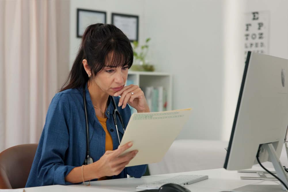 Reading, doctor and woman in office with computer for patient review, medical research or diagnosis. Healthcare, clinic and mature person with document, report and online results for telehealth